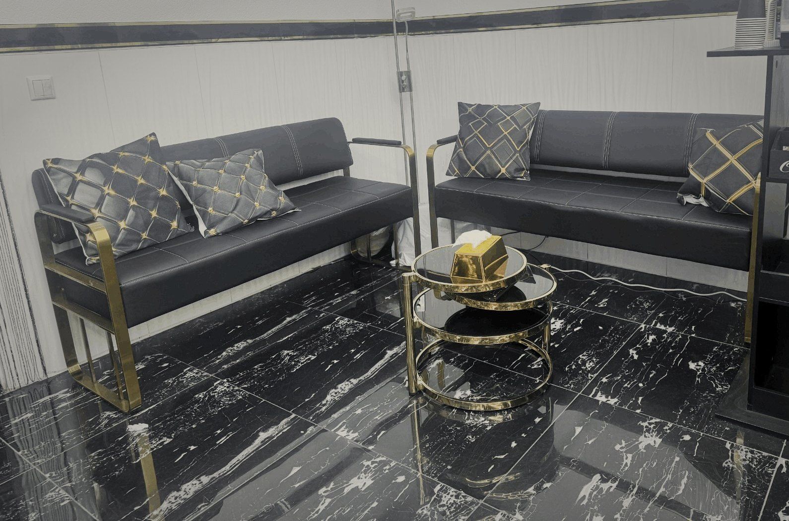 Wartebereich mit schwarzen Ledersofas, goldenem Couchtisch und Kaffeemaschine